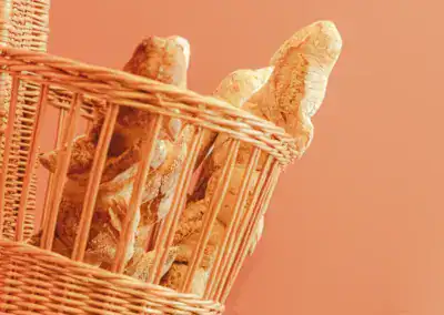 Mehrere Baguette-Brote in einem Weidenkorb vor einem warmen pfirsichfarbenen Hintergrund.