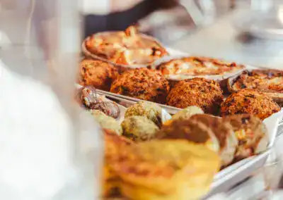 Eine Nahaufnahme von verschiedenen Backwaren, darunter Muffins, Kuchen und Gebäck, die auf Tabletts in einer Bäckerei ausgestellt sind. Die Leckereien sind goldbraun und sehen frisch gebacken aus.