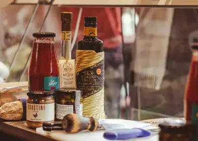 Eine Auswahl an italienischen Lebensmitteln, darunter Olivenöl, Balsamico-Essig, Tomatensoße und Brotaufstriche, die auf einem Küchentisch angeordnet sind, wobei ein Messer und Brot in der Nähe liegen.